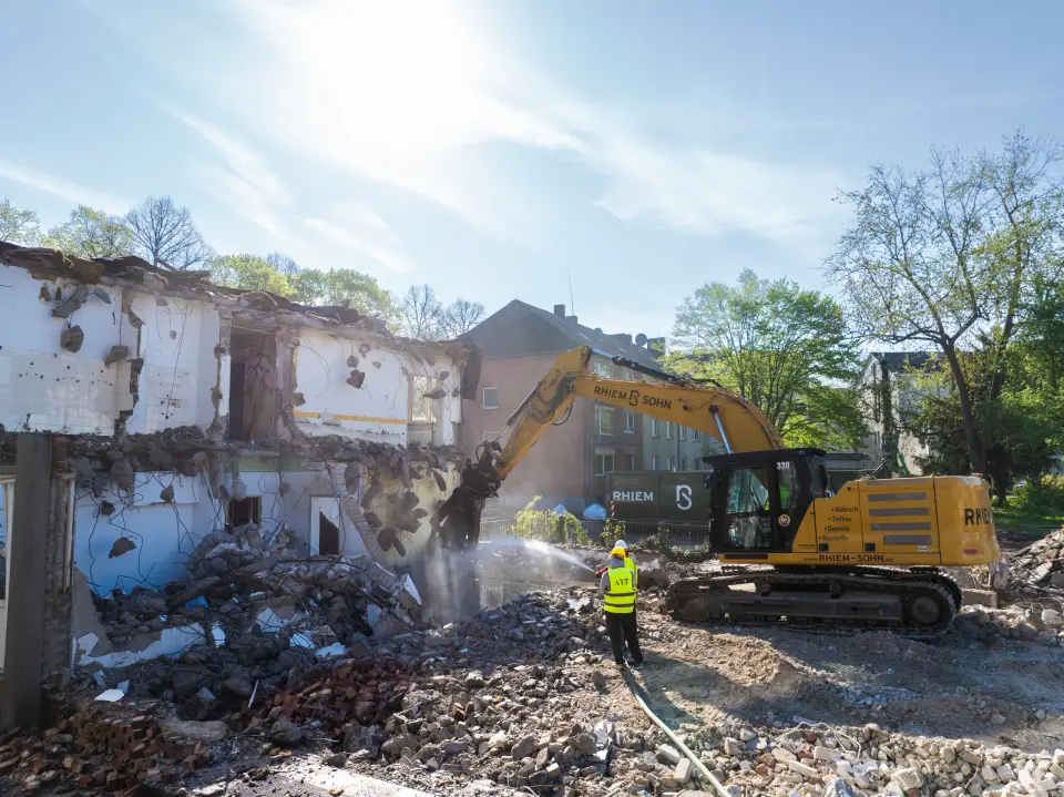 Bagger beim Abriss eines Altbaus der Aachener SWG, Arbeiter mit Warnweste stehen daneben