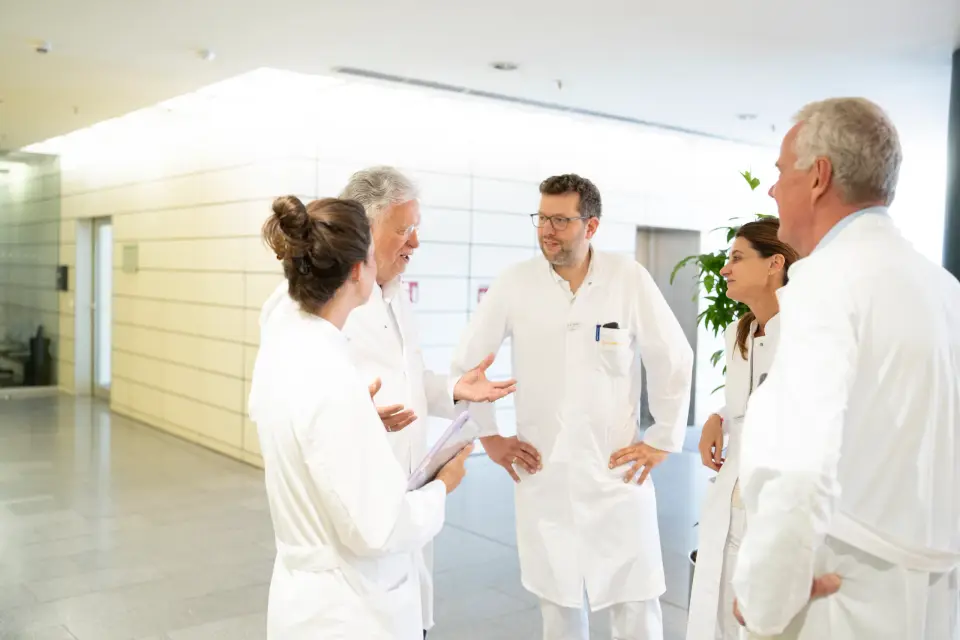 Ärztinnen und Ärzte in weißen Kitteln im Gespräch im hellen Flur der Pan Klinik in Köln