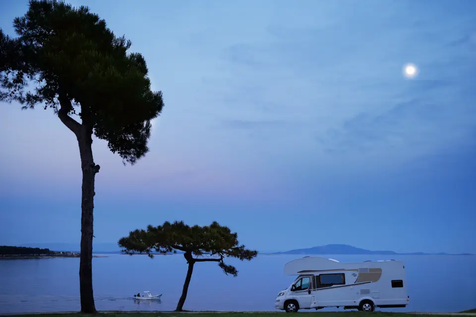 Das Carado Alkoven Wohnmobil A461 steht zur blauen Stunde unter Pinien am Meer