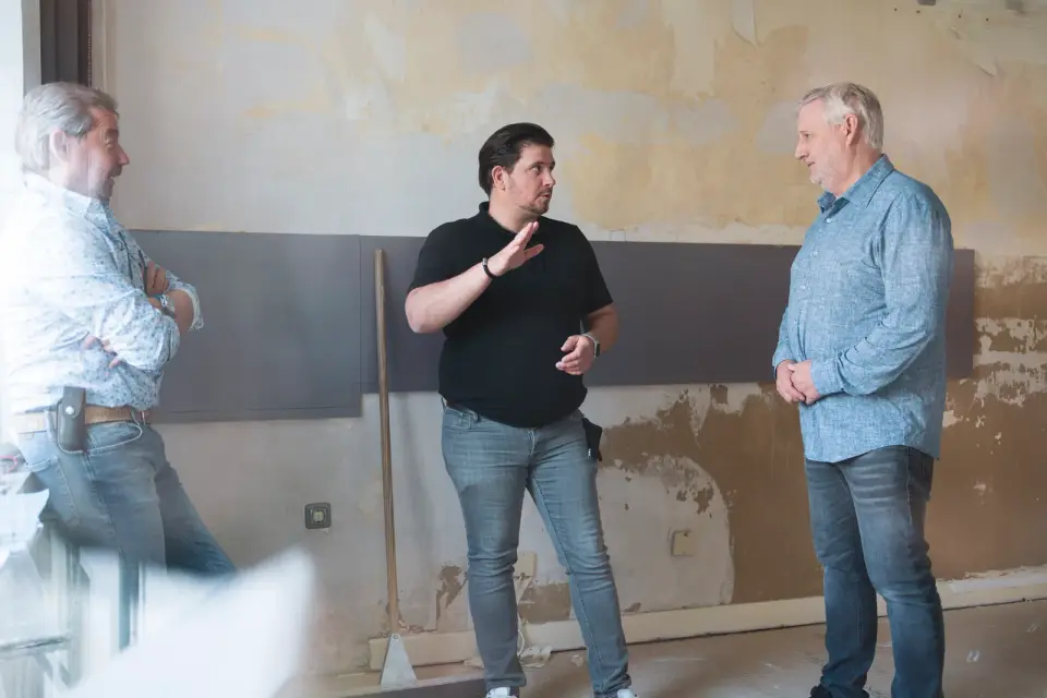 Mitarbeiter der GWG zu Köln besprechen sich in einer Wohnung, deren Wände für die Sanierung freigelegt sind.