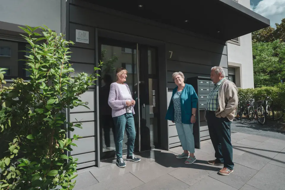 Drei ältere Bewohner der GWG zu Köln unterhalten sich vor dem modernisierten Hauseingang ihres Wohnhauses.