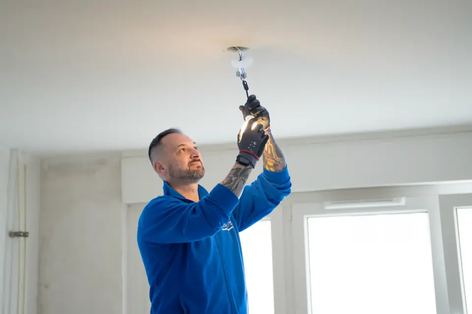Ein Elektriker der GWG Rhein-Erft montiert bei der Renovierung einer leeren Wohnung im Rhein-Erft-Kreis einen Deckenanschluss.