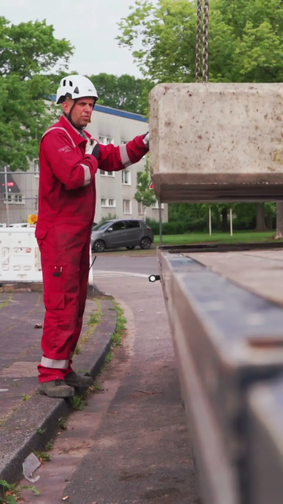 Ein Monteur in rotem Overall führt bei der Kranaufstellung auf der Baustelle der GAG Immobilien in Köln-Stammheim einen schwebenden Betonballast.