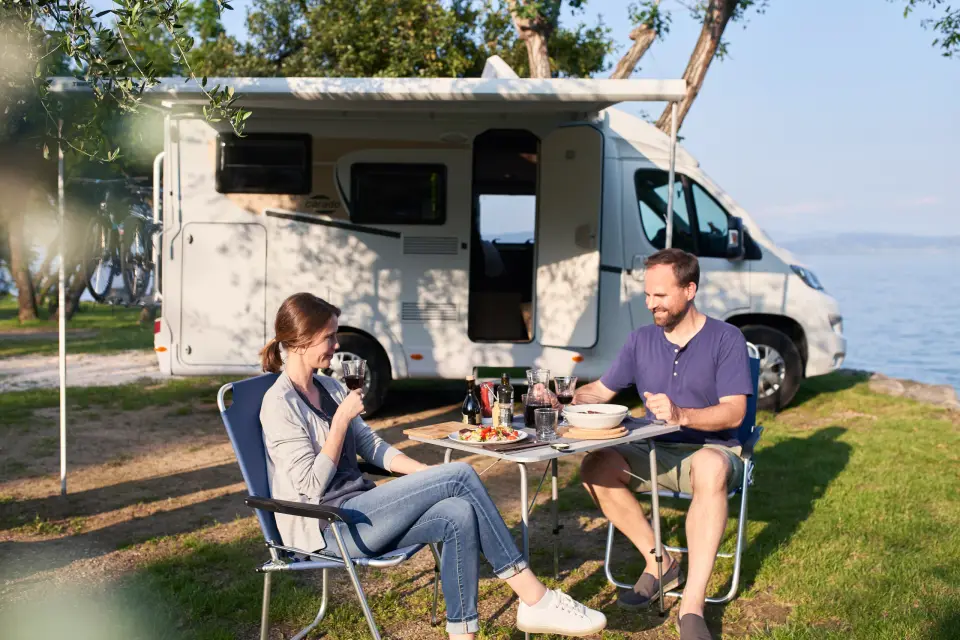 Ein Paar sitzt beim Frühstück am Campingtisch vor dem Carado Van V132