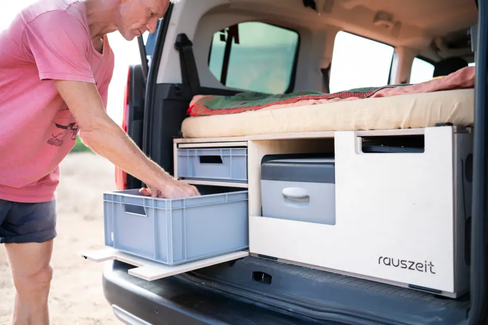 Ein Mann zieht eine Kiste aus dem Schubfach der Rauszeit Campingbox im Heck des Autos