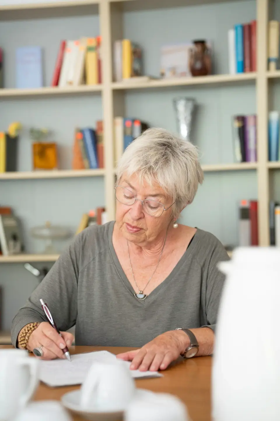 Eine ältere Teilnehmerin mit Brille schreibt konzentriert an ihrem Text in der Schreibwerkstatt Zuhause mit Plus der GAG Immobilien.