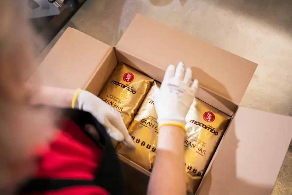 Mitarbeiterin mit Handschuhen packt goldene Kaffeebeutel in einen Versandkarton bei Drago Mocambo in Radevormwald